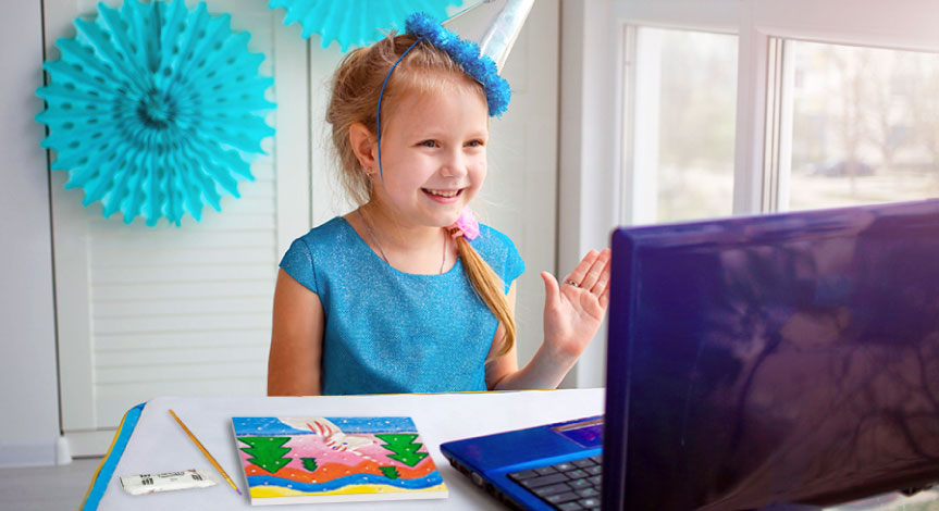 Girl wearing a birthday hat raising hand while working in front of her purple computer with a picture of a unicorn next to he